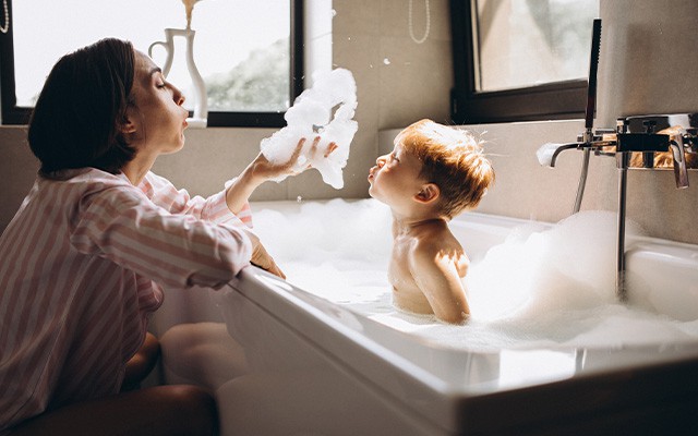 Mutter und Kind pusten in den Schaum der Badewanne